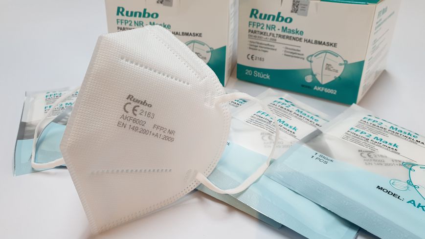 Die Verpackung unserer FFP2 Masken und eine Puppe mit angelegter FFP2 Maske